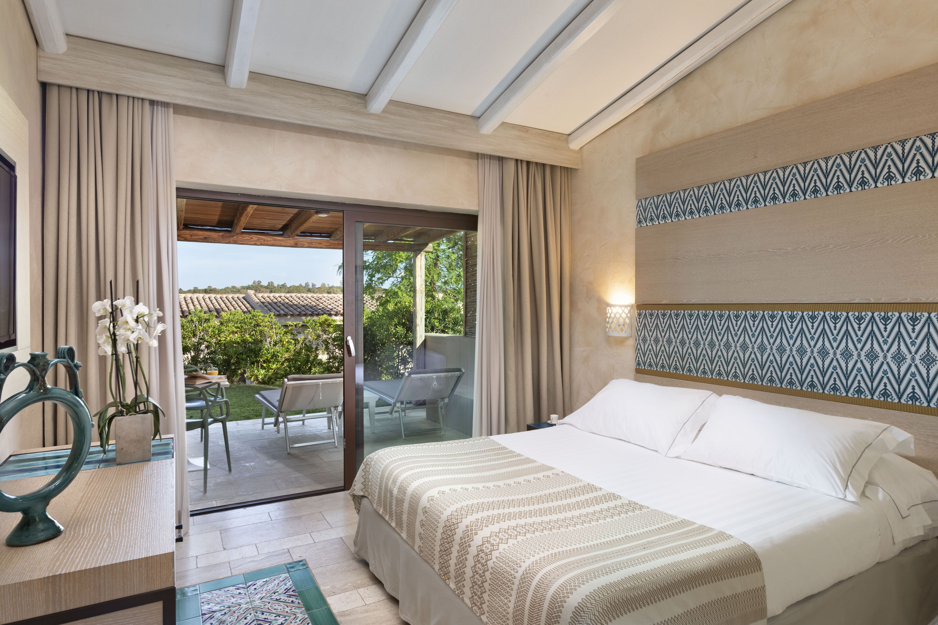 A hotel room with a bed, a desk, a chair, a small table, and a view of the outdoors.