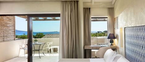 Una habitación de hotel moderna con balcón, cama, escritorio y vista al mar.