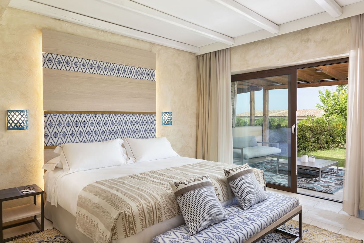 Una habitación de hotel moderna con una cama grande, un sofá y una puerta corrediza de vidrio que da a un patio exterior.
