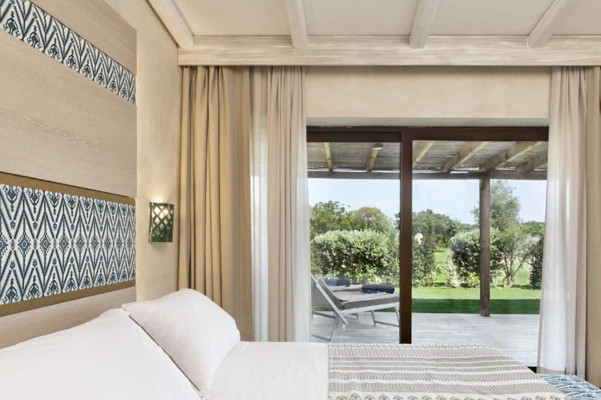 Un dormitorio con cama, pared decorada y vista a un espacio exterior con una silla y follaje.