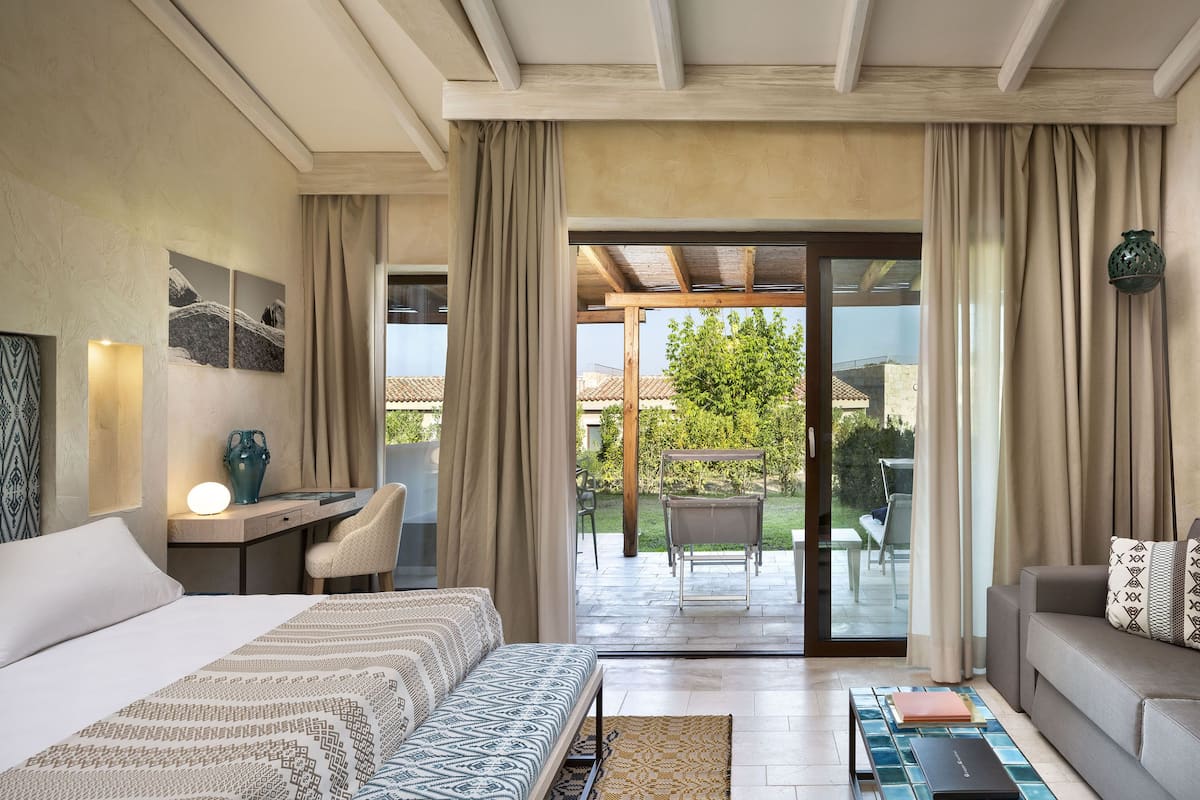 Habitación de hotel con cama, escritorio, silla, sofá y vista al patio exterior.