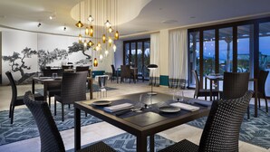 A dining area with a table set for two, surrounded by wicker chairs, a large window with curtains, and a hanging light fixture. - Baglioni Resort Sardinia - The Leading Hotels of the World (San Teodoro)
