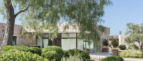A modern building with stone walls and large windows, surrounded by well-maintained gardens and trees.