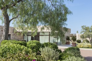 A modern building with stone walls and large windows, surrounded by well-maintained gardens and trees.