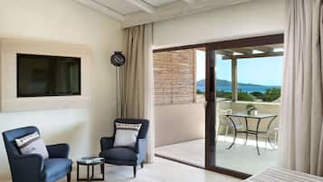 A living room with two armchairs, a small table, and a TV mounted on the wall. There is a sliding glass door leading to an outdoor area with a table and chairs.