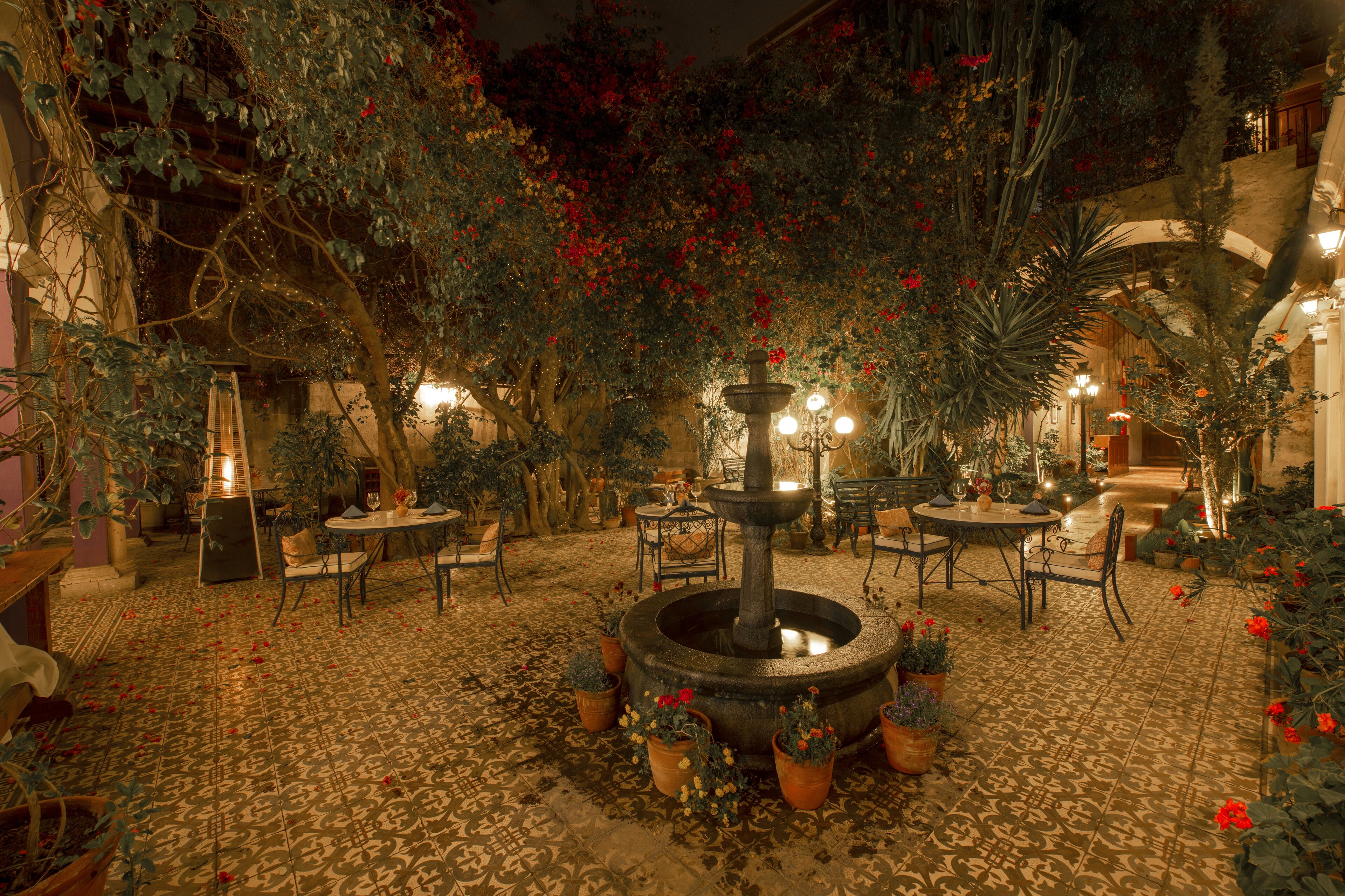 Un patio interior con una fuente central, plantas en macetas y mobiliario exterior.