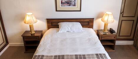 A neatly made bed with a plaid blanket, two bedside lamps, a framed picture on the wall, and a wooden headboard.