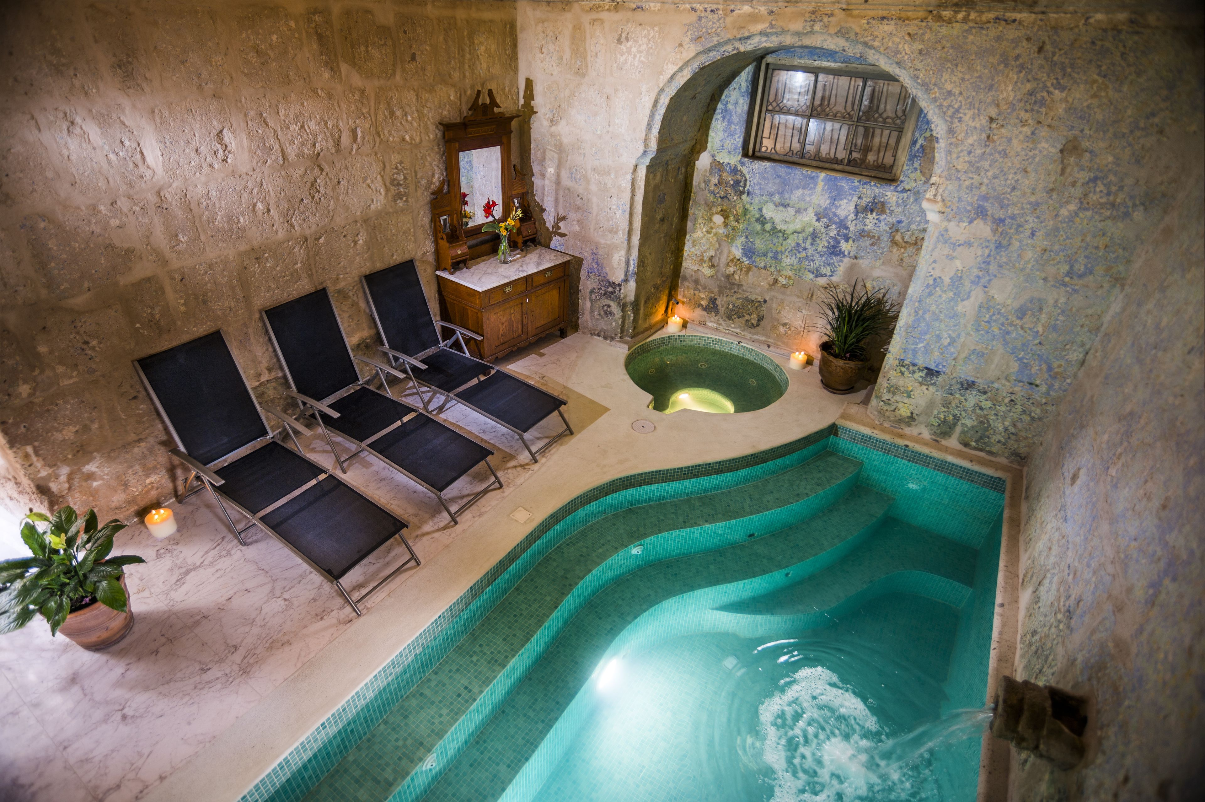 Zona de spa con un jacuzzi pequeño, sillones de descanso y una pared de piedra.