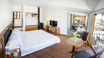 Habitación de hotel con cama, escritorio, televisión, balcón con vistas y baño con espejo y lavamanos.