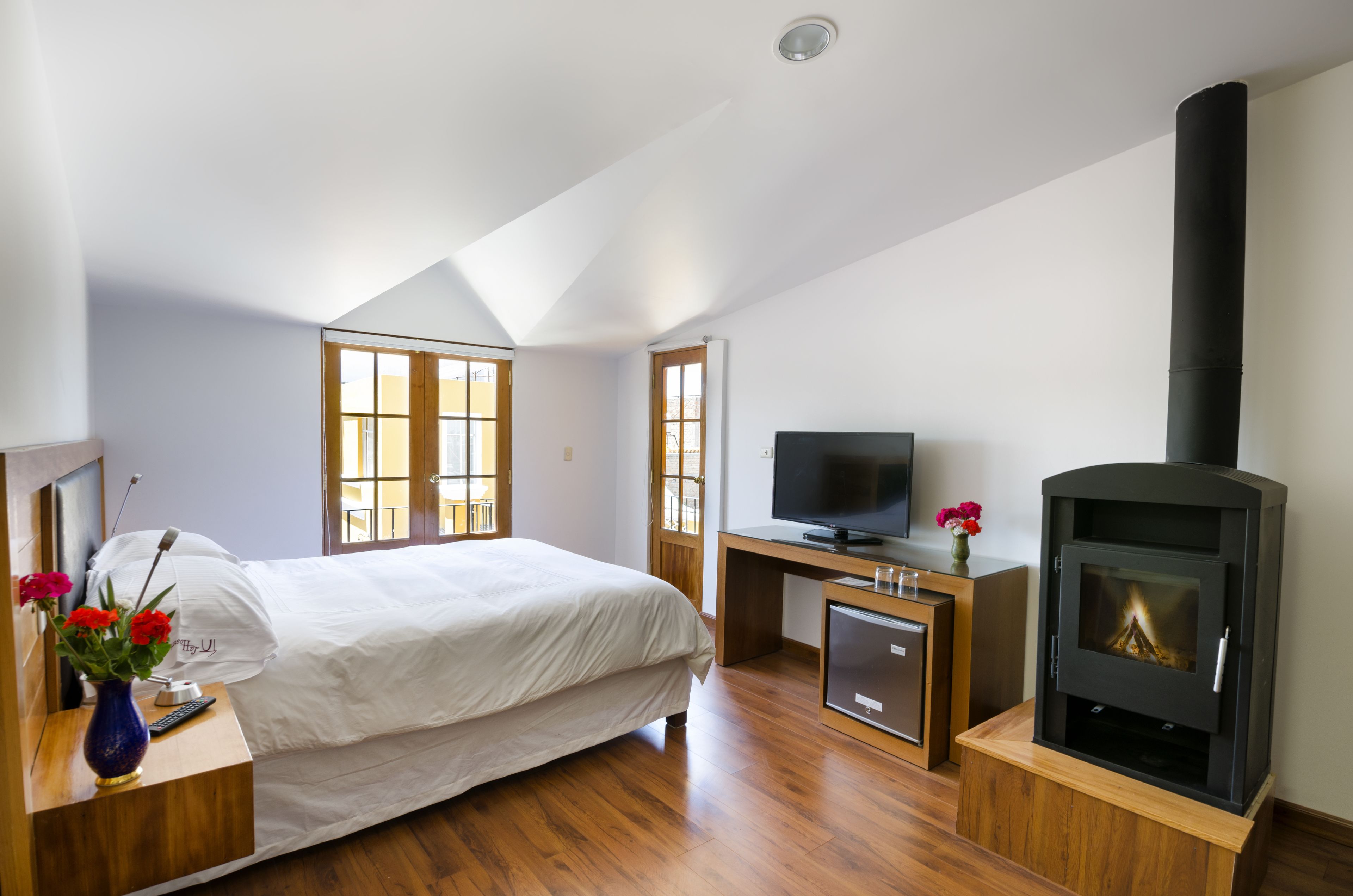 Un dormitorio con cama, escritorio con televisor, mueble pequeño, chimenea y ventana.
