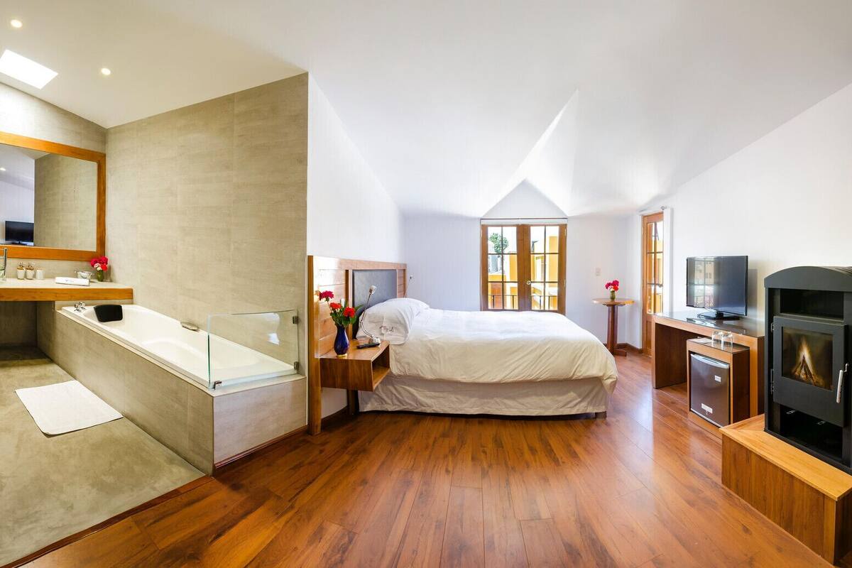 Un dormitorio moderno con una cama grande, suelo de madera, televisor integrado y chimenea.
