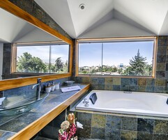 Un baño moderno con una bañera grande, un tocador de madera y vistas de la ciudad a través de un ventanal amplio.