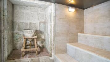 Zona de ducha con paredes de piedra, un taburete de madera y una lámpara.