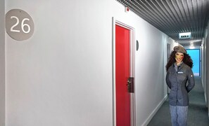 A hotel corridor with a red door, a number '26' sign, and a person in a uniform. - Hotel João XXI (Braga)