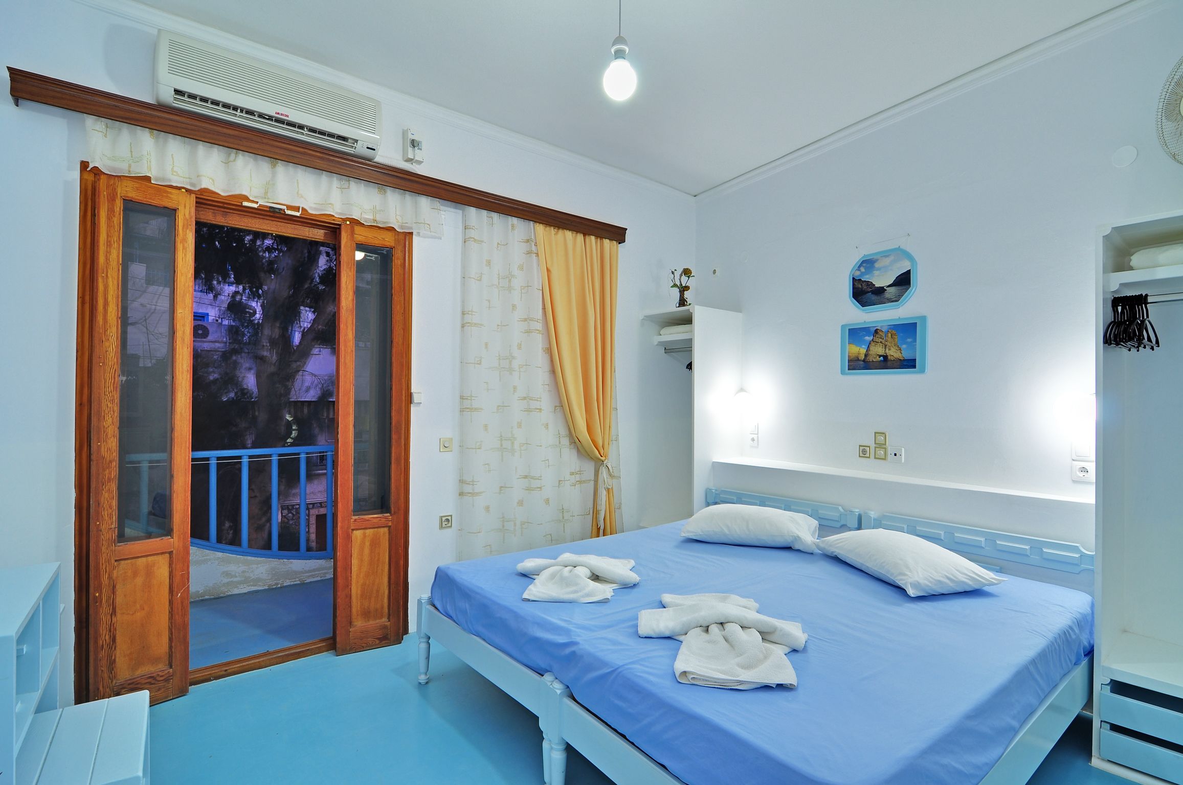 A bedroom with a bed, a window with curtains, a wall-mounted air conditioner, and a ceiling light.