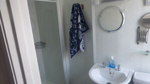 Une salle de bain avec un lavabo blanc, un miroir, une serviette et une douche.