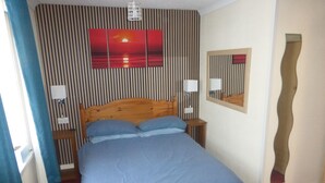 Une chambre à coucher avec un lit, des lampes de chevet, un miroir et un mur à rayures verticales.