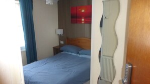 Une chambre à coucher comprenant un lit, une table de chevet, une lampe fixée au mur, un miroir et un radiateur.