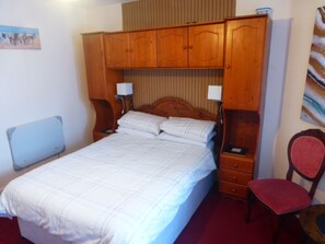 Un dormitorio con una cama, dos mesitas de noche, una silla y armarios de madera sobre la cama.