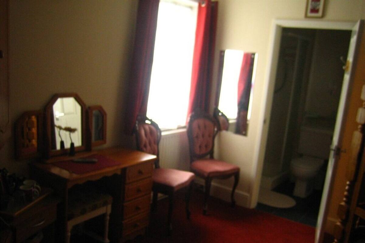 A bedroom with a wooden dresser, a chair, a desk, and a window with curtains.