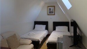 Una habitación pequeña y bien iluminada con dos camas, un sofá y un televisor.