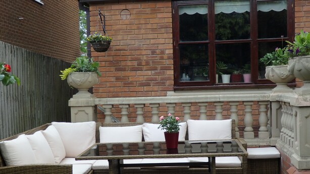 Un conjunto de sillones de mimbre con cojines, una mesa con superficie de vidrio y plantas en macetas.