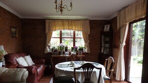 Una sala de estar acogedora con pared de ladrillo, un sofá de cuero, una mesa de comedor con sillas y un amplio ventanal con cortinas.