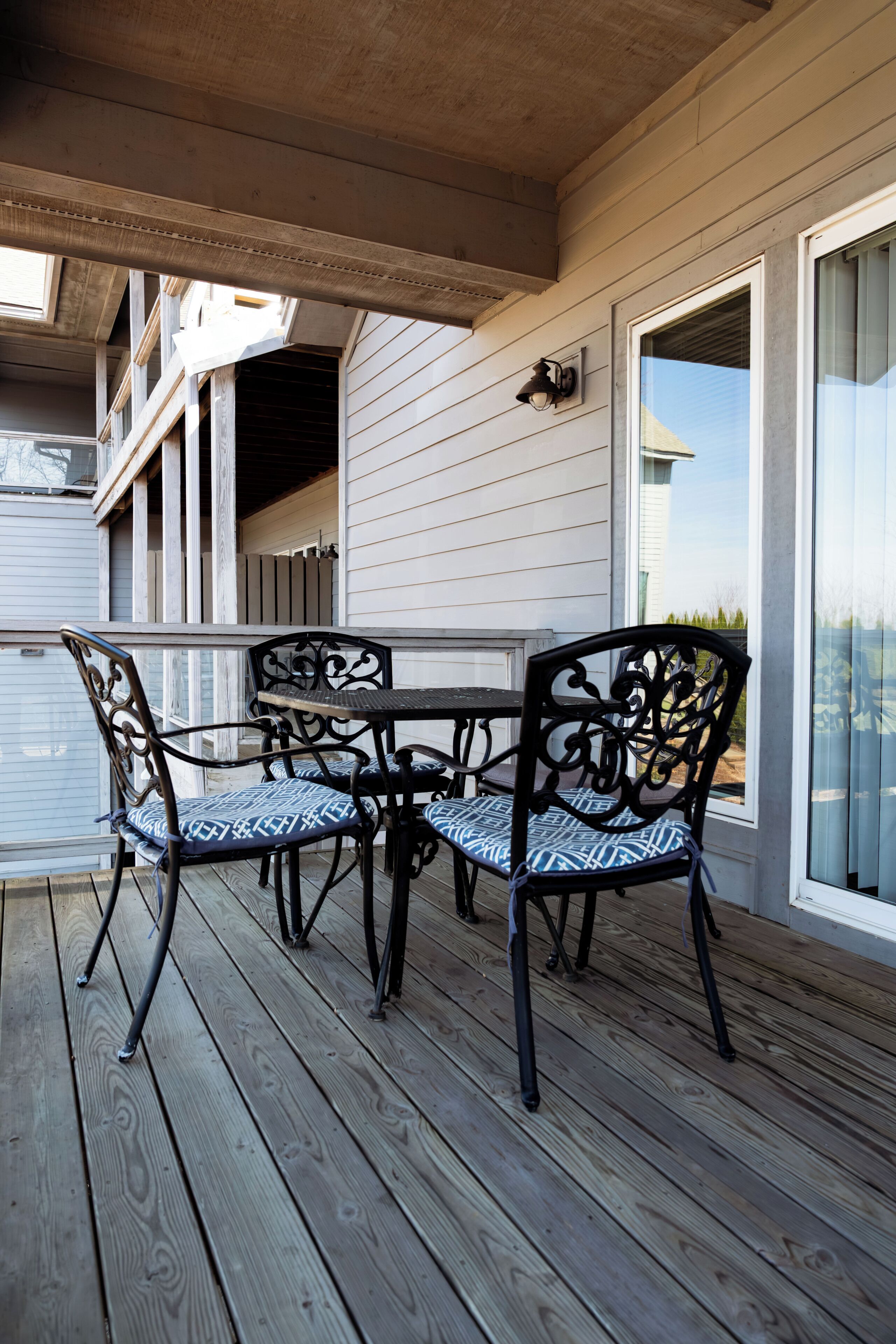 Un patio cubierto al aire libre con mesa y sillas, terraza de madera y vista a un edificio con grandes ventanales.