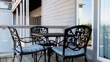 Un patio cubierto al aire libre con mesa y sillas, terraza de madera y vista a un edificio con grandes ventanales.