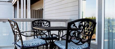 Un patio cubierto al aire libre con mesa y sillas, terraza de madera y vista a un edificio con grandes ventanales.