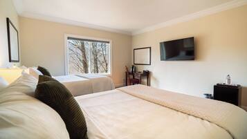 A hotel room with two beds, a TV, a window with a view of trees, and a desk with a chair.