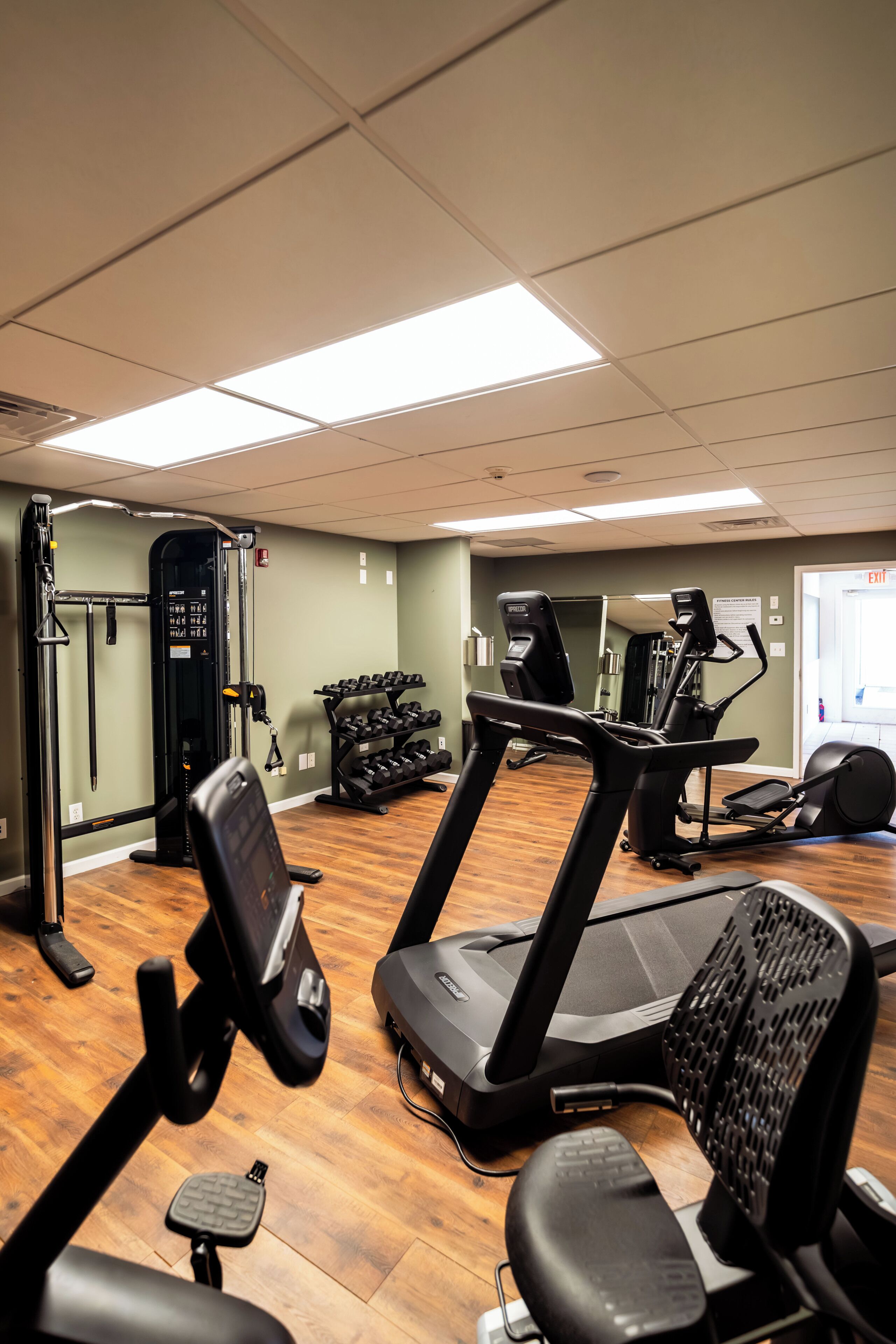 A gym with exercise equipment, a mirror, and a door with an exit sign.