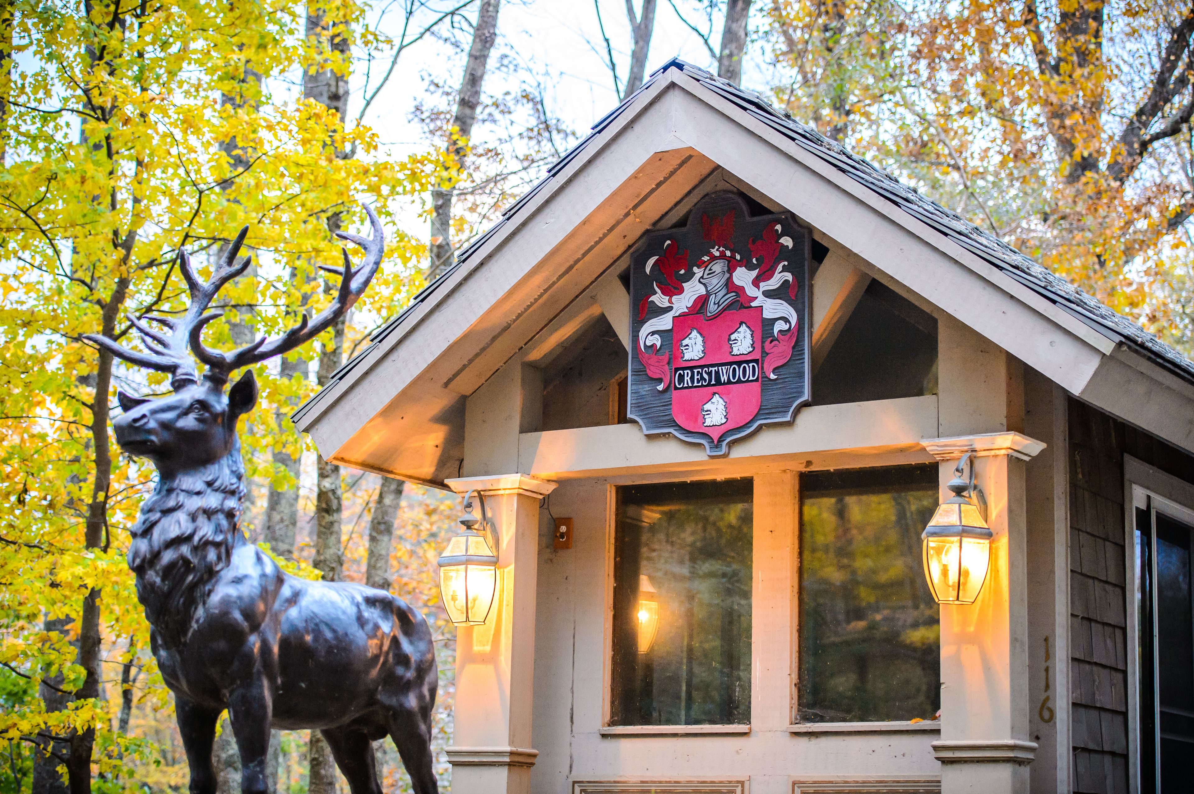 A lodge with a crest sign, a deer statue, and two lit lanterns.