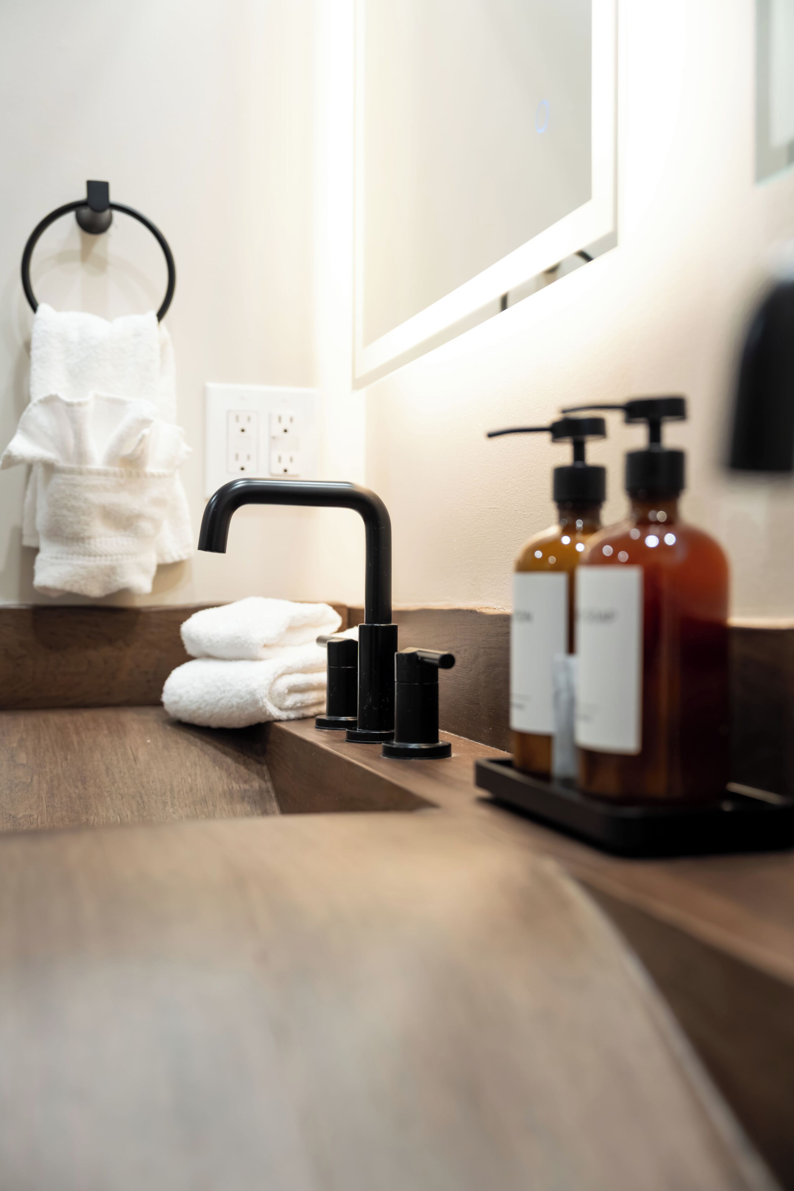 A bathroom with a wooden countertop, a black faucet, two bottles of liquid soap, and a white towel hanging on a ring.