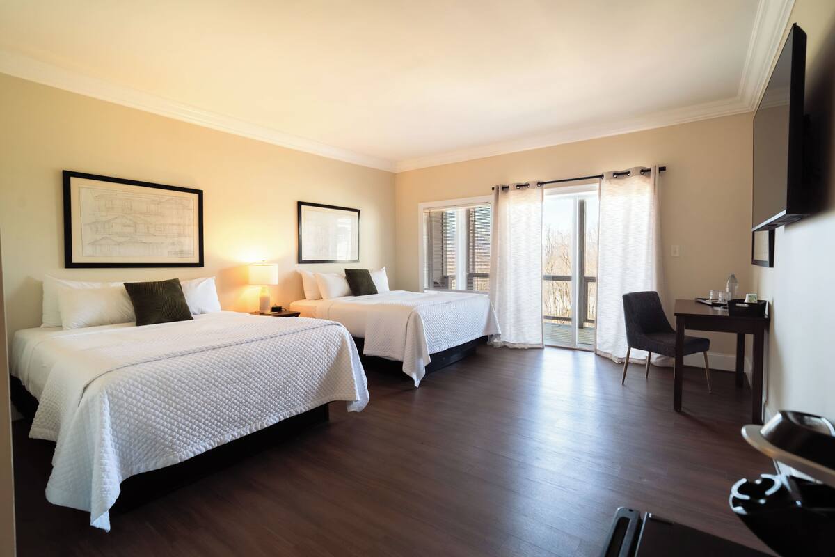 A hotel room with two beds, a desk, a chair, a TV, and a balcony with curtains.