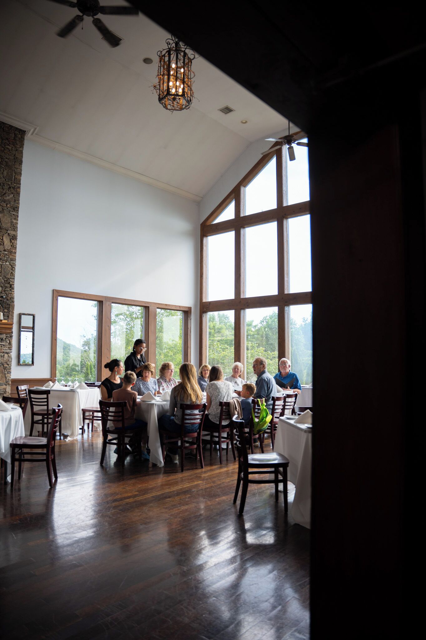 A dining area with large windows, wooden floors, and a chandelier.