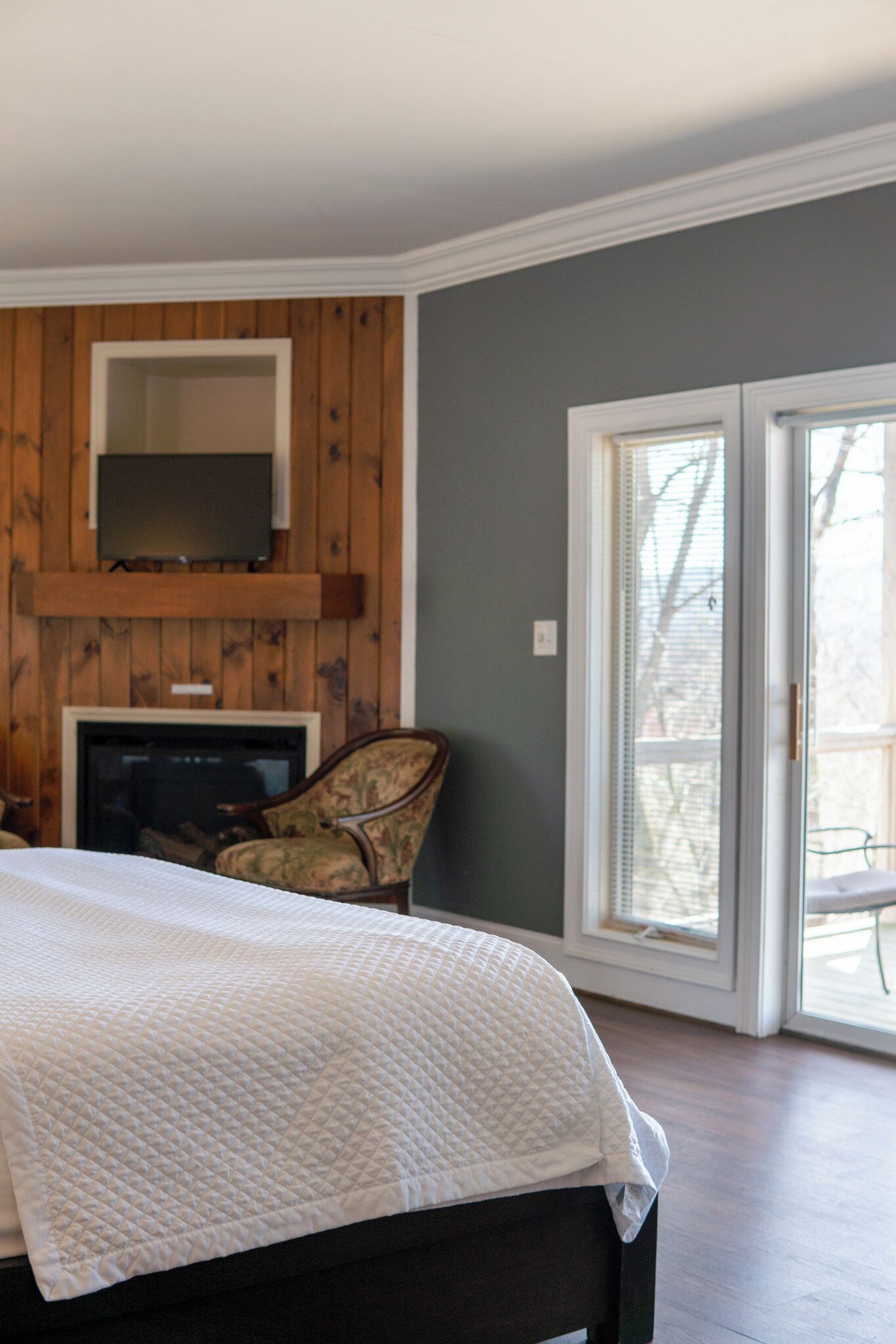 A bedroom with a bed, a television mounted on a wooden wall, a fireplace, and a sliding glass door leading to an outdoor area.