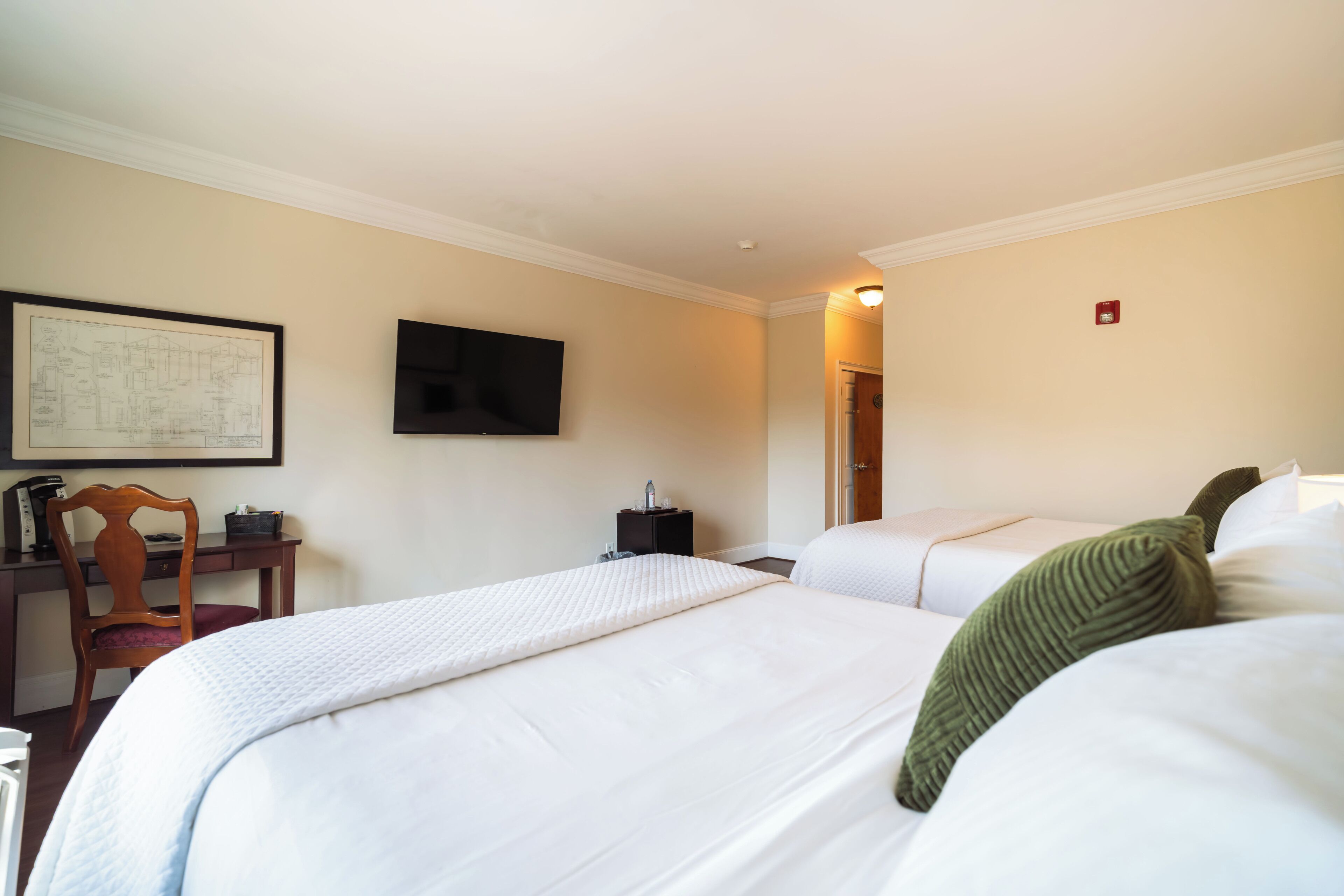 A hotel room with a large bed, a desk with a chair, a flat-screen TV, and a framed picture on the wall.