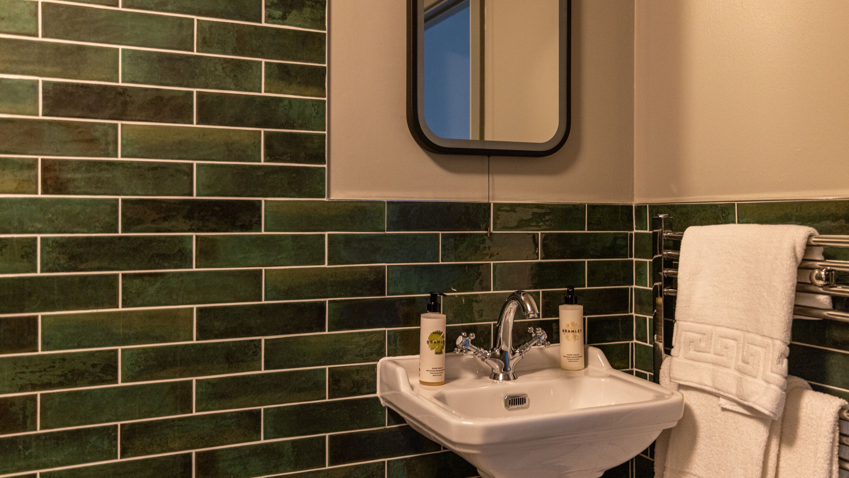 A bathroom with a white sink, green tiled backsplash, a mirror, and a towel rack.