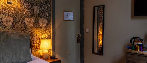 A hotel room with a bed, a nightstand with a lamp, a wall clock, a door with a map, and a mirror.