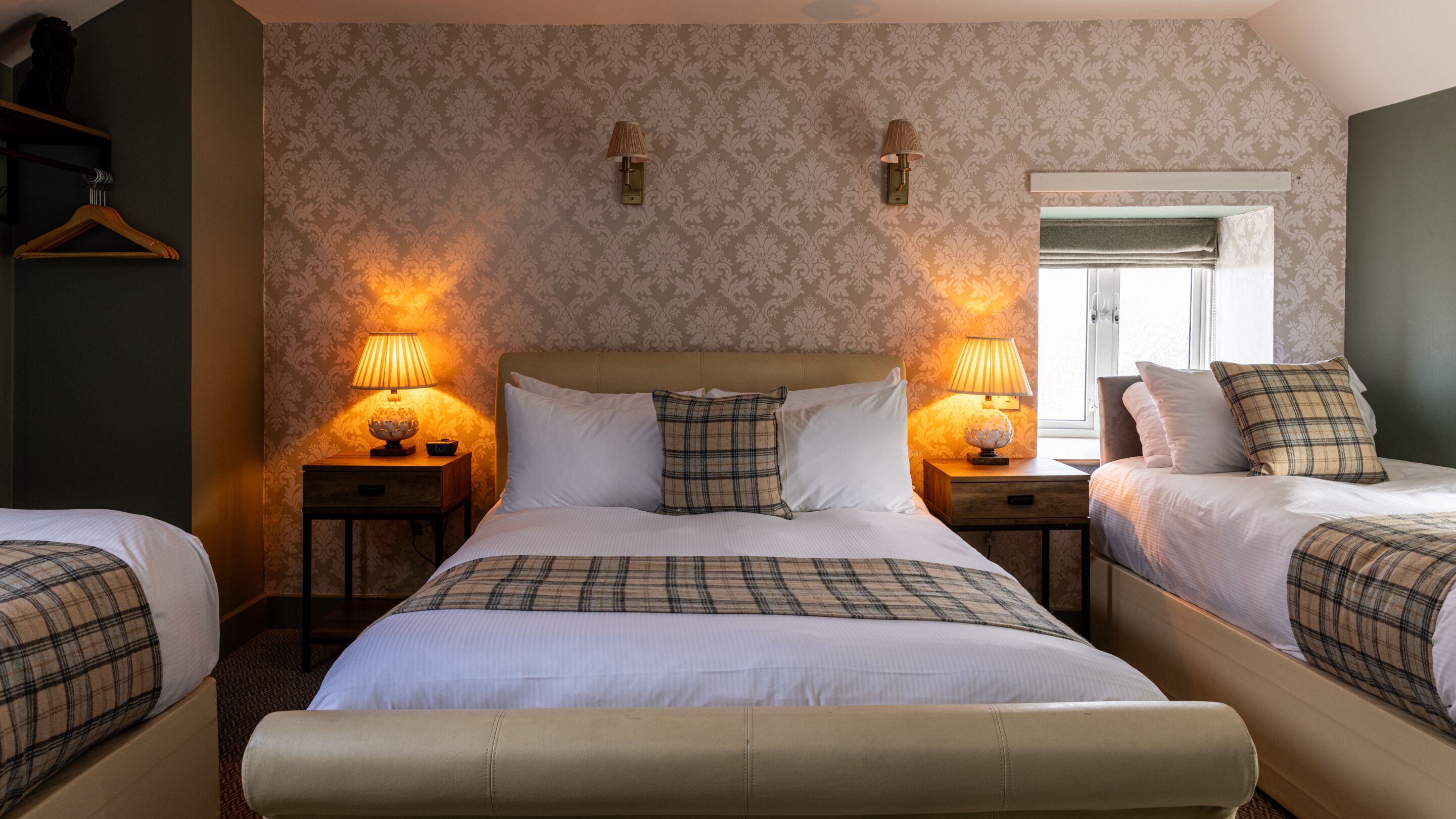 A hotel room with a large bed, two bedside tables with lamps, a window with a view, and a patterned wallpaper.