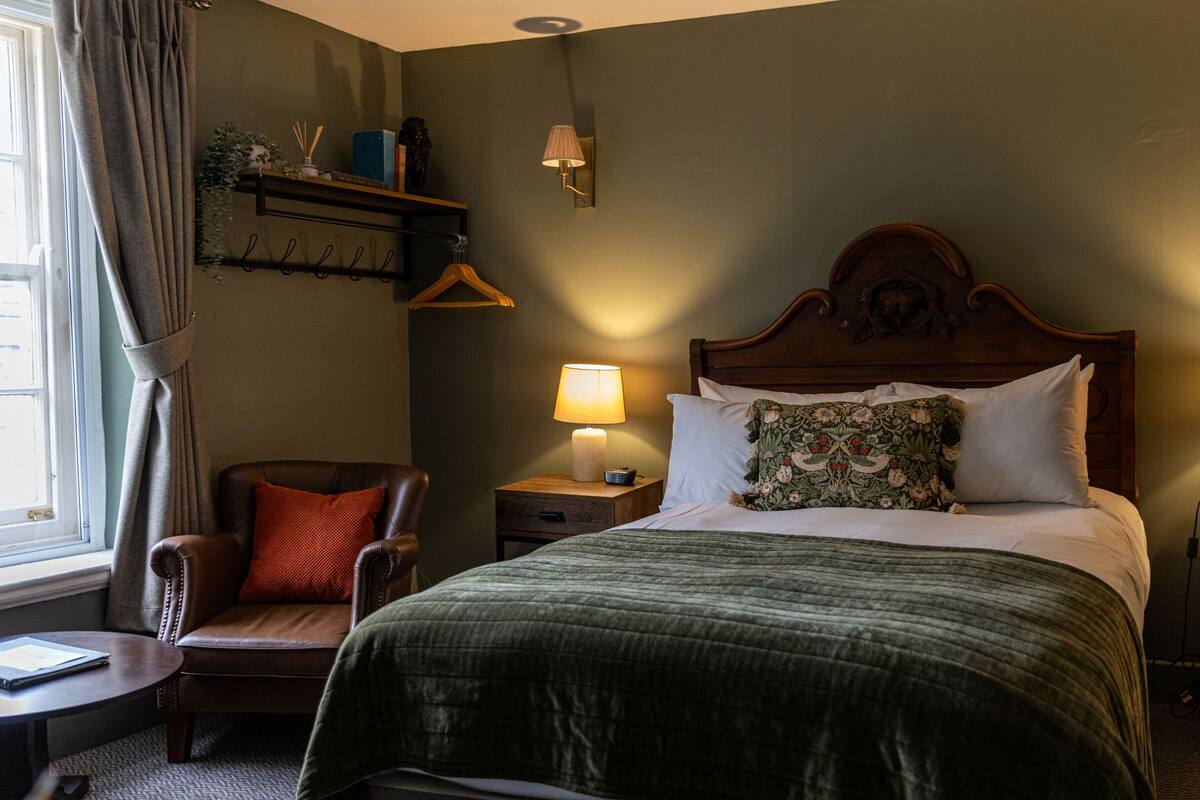 Een slaapkamer met een groot bed, twee nachtkastjes, een stoel, een lamp en een raam met gordijnen.