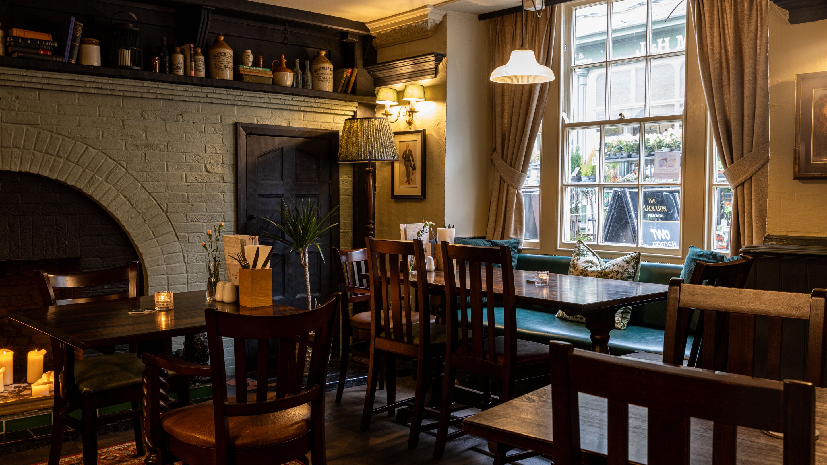 A cozy pub with a brick fireplace, wooden furniture, and a view of the street outside.