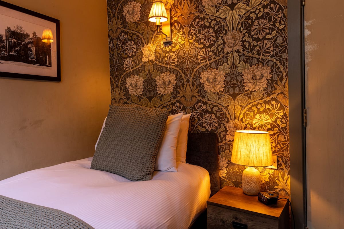 Een net opgemaakt bed met kussens, een inlijsting foto aan de muur en twee wandlampen.