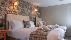 Een hotelkamer met een groot bed, twee nachtkastjes, bloemenbehang en wandlampen.
