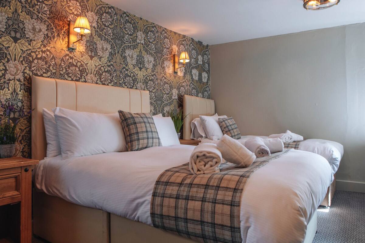 Een hotelkamer met een groot bed, twee nachtkastjes, bloemenbehang en wandlampen.