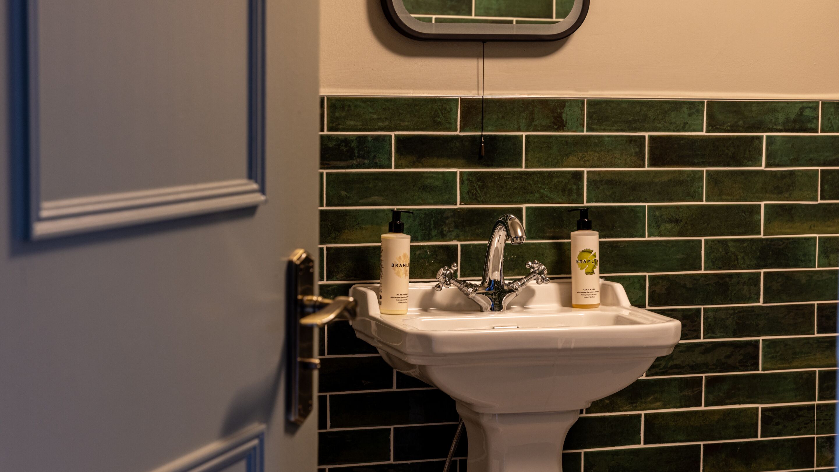 A bathroom with a white sink, two bottles of hand soap, and a green-tiled wall.