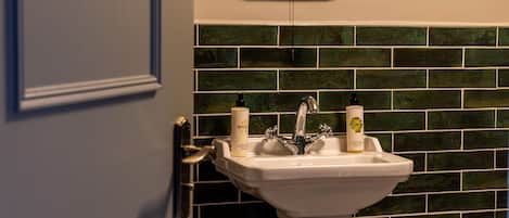 Un baño con un lavamanos blanco, dos jabones para manos y una pared de azulejos verdes.