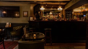 Een bar met een toonbank waarop verschillende flessen staan, een bord met de tekst 'THE BLACKPOLLON' en een groot ingelijst schilderij aan de muur.