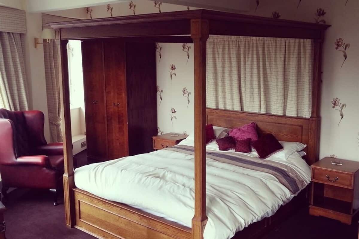A four-poster bed with a wooden frame, a nightstand, a chair, and a wardrobe.